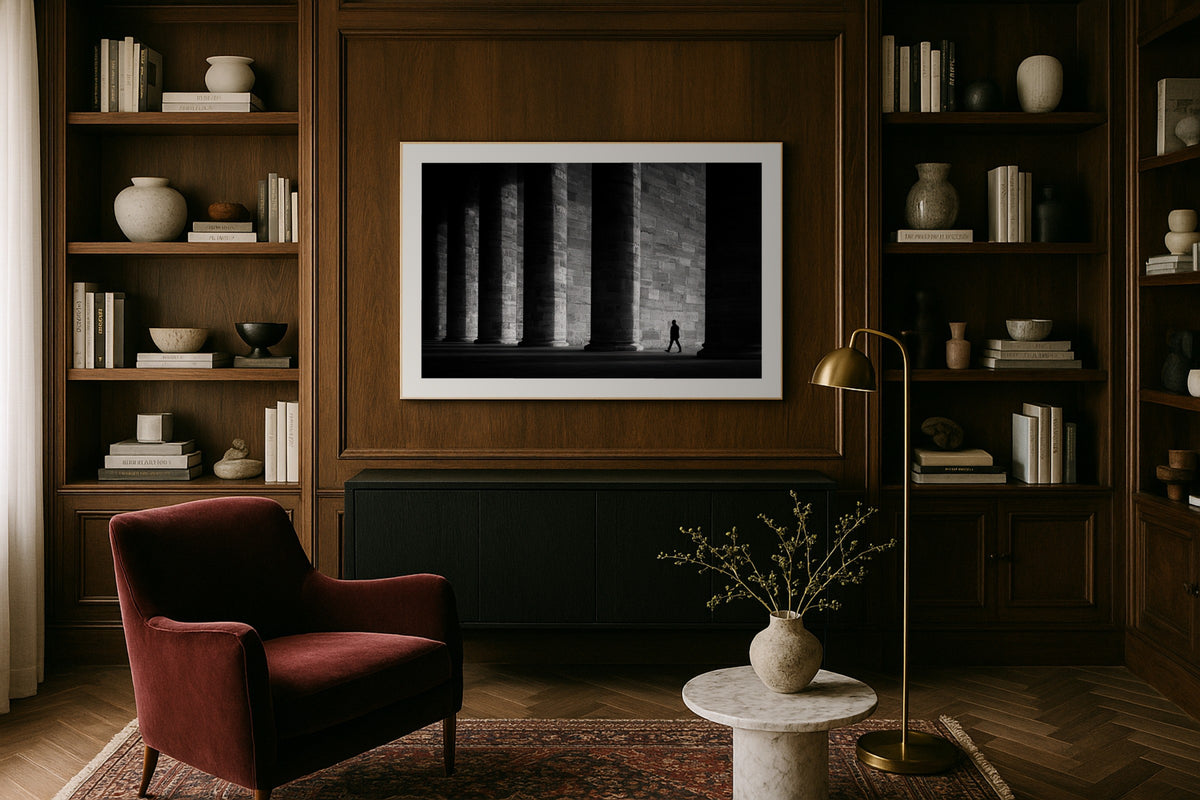 Figure in the Colonnade wall art print, framed with a white border, in a library wood panels velvet chair